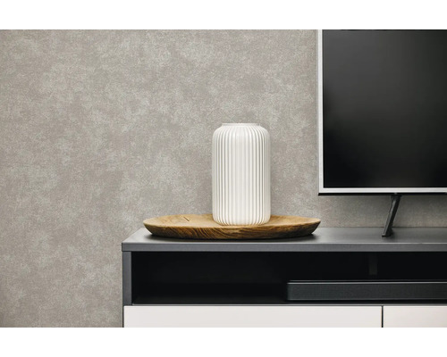 Vliesbehang in grijze betonlook achter een dressoir met een witte vaas op een houten dienblad en een televisie.