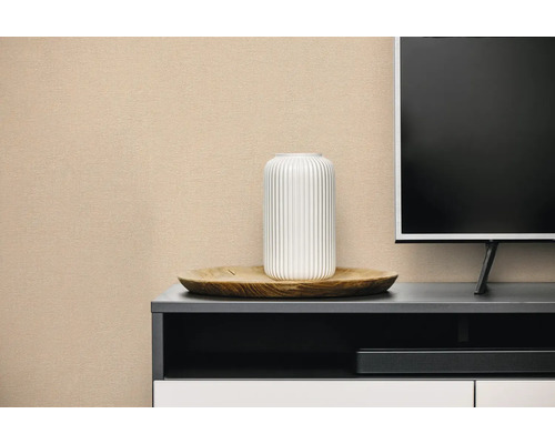 Gestructureerd behang op een muur in een lichte woonkamer achter een tv-meubel met een witte vaas en een houten schaal.