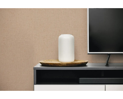 Beige vliesbehang met linnenstructuur op een muur in een moderne woonkamer achter een dressoir.