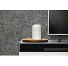 Donkergrijs vliesbehang met licht boompatroon achter een modern tv-meubel met decoratieve vaas en televisie.