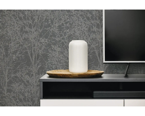 Donkergrijs vliesbehang met licht boompatroon achter een modern tv-meubel met decoratieve vaas en televisie.