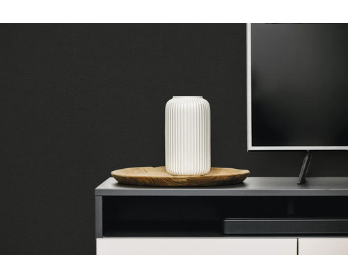Moderne woonkamer met een zwarte wand met textuur, een witte geribbelde vaas op een houten dienblad en een donker tv-meubel.