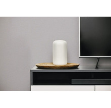Witte geribbelde vaas op een houten dienblad op een modern tv-meubel naast een televisie.
