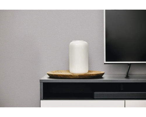 Witte geribbelde vaas op een houten dienblad op een modern tv-meubel naast een televisie.
