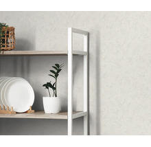 Lichtgrijs vliesbehang met fijne structuur achter een wit rek met houten planken, borden en een plant.