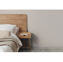 Moderne slaapkamer met houten hoofdbord, klein houten nachtkastje met lade en een bed met lichtgekleurd beddengoed.