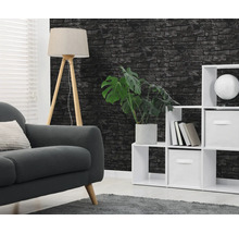 Vliesbehang met zwart baksteenmotief in een woonkamer met grijze bank, witte vakkenkast en houten statiefvloerlamp.
