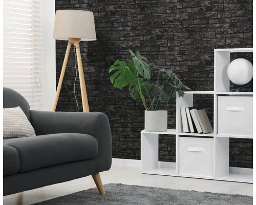 Vliesbehang met zwart baksteenmotief in een woonkamer met grijze bank, witte vakkenkast en houten statiefvloerlamp.