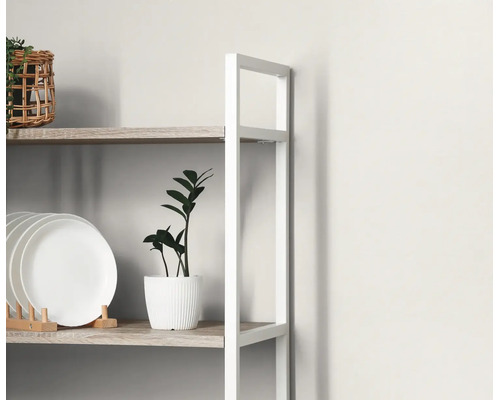 Detail van een modern opbergrek met een wit metalen frame en houten planken, met een bordenrek en een kleine kamerplant.