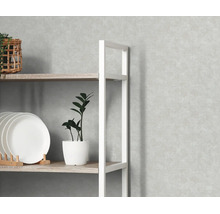 Lichtgrijs vliesbehang met betonlook op een wand achter een houten stellingkast met wit metalen frame.
