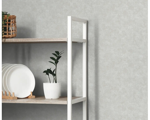 Lichtgrijs vliesbehang met betonlook op een wand achter een houten stellingkast met wit metalen frame.