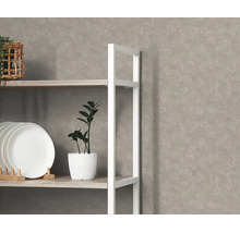 Gestructureerd vliesbehang met betonlook op een wand achter een georganiseerd wit rek met borden en een plant.