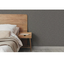 Donkergrijs vliesbehang met fijne structuur in een slaapkamer met houten hoofdbord en nachtkastje.