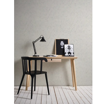 Werkplek met een licht houten bureau, zwarte stoel en lamp voor een muur met structuur en stucwerk-effect en een witte houten vloer.
