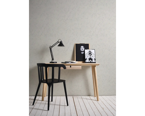 Werkplek met een licht houten bureau, zwarte stoel en lamp voor een muur met structuur en stucwerk-effect en een witte houten vloer.