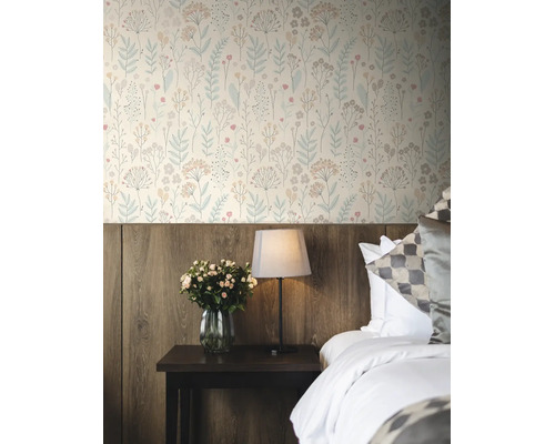 Vliesbehang met floraal patroon in een slaapkamer boven een houten lambrisering, naast een nachtkastje met lamp en bloemen.