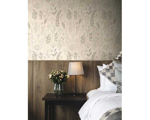 Vliesbehang met bloemenpatroon in een slaapkamer boven een houten wandpaneel met nachtkastje, lamp en bloemen.