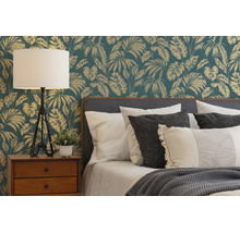 Slaapkamer met jungle-vliesbehang met bladerenpatroon achter een bed met kussens, houten nachtkastje en een tafellamp.