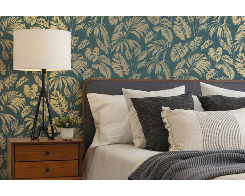 Slaapkamer met jungle-vliesbehang met bladerenpatroon achter een bed met kussens, houten nachtkastje en een tafellamp.