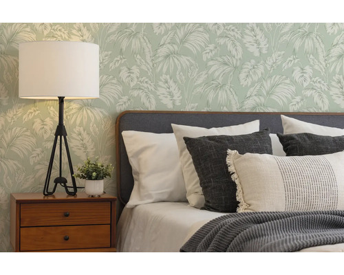 Vliesbehang met palmbladeren in een lichte slaapkamer met grijs gestoffeerd bed, houten nachtkastje en een tafellamp met statiefontwerp.