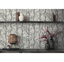 Vliesbehang met zwart boom- en takkenpatroon op een lichte achtergrond, gedecoreerd met een donkere wandplank, vazen, kaarsen en een houten lantaarn.