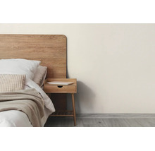 Lichte slaapkamer met een bed met houten hoofdbord, witte kussens en beige deken naast een houten nachtkastje op een grijze vloer.
