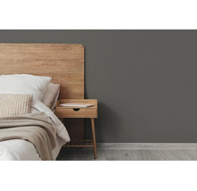 Moderne slaapkamer met donkergrijze muurverf, houten hoofdbord, houten nachtkastje en licht textiel.