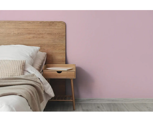 Slaapkamer met lila muur, bed met houten hoofdbord en houten nachtkastje op een lichte houten vloer.