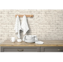 Vliesbehang met steenlook en licht baksteenpatroon op een keukenmuur boven een houten werkblad met servies.