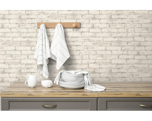 Vliesbehang met steenlook en licht baksteenpatroon op een keukenmuur boven een houten werkblad met servies.