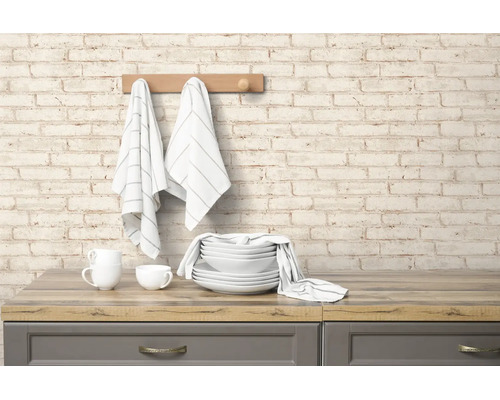 Vliesbehang met baksteenmotief op een keukenmuur boven een houten werkblad met servies en handdoeken.