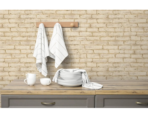 Vliesbehang in baksteenlook op een keukenmuur met hangende theedoeken en servies op een aanrechtblad in houtlook.