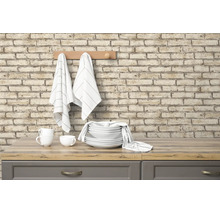 Lichte, georganiseerde keuken met muur in baksteenlook, houten werkblad, wit servies en keukendoeken aan een houten kapstok.