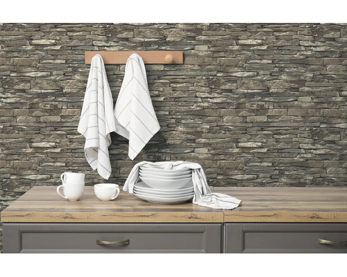 Moderne keuken met vliesbehang in steenoptiek op de muur, gecombineerd met een licht werkblad in houtoptiek en wit keramisch servies.