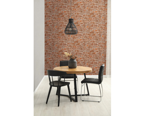 Woonkamer met behang in baksteenlook, ronde houten tafel en zwarte stoelen.
