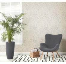 Lichte woonkamer met vliesbehang met botanisch patroon, een grote kamerplant in een grijze pot, een fauteuil en een vloerkleed met patroon.