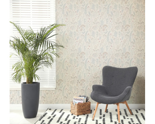 Lichte woonkamer met vliesbehang met botanisch patroon, een grote kamerplant in een grijze pot, een fauteuil en een vloerkleed met patroon.