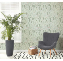 Lichte woonkamer met botanisch behang, grijze fauteuil, grote kamerplant en een vloerkleed met patroon bij een raam met jaloezieën.