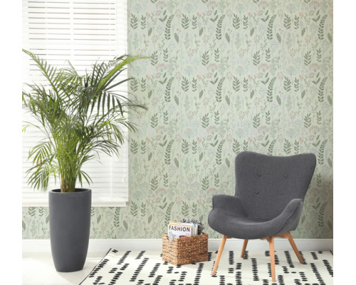 Lichte woonkamer met botanisch behang, grijze fauteuil, grote kamerplant en een vloerkleed met patroon bij een raam met jaloezieën.