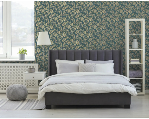 Vliesbehang met goudkleurig palmbladpatroon achter een grijs gestoffeerd bed in een moderne, lichte slaapkamer.
