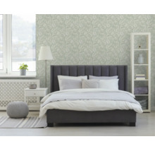 Moderne slaapkamer met donkergrijs gestoffeerd bed, wit beddengoed en licht behang met bladmotief op de muur.