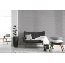 Grijs vliesbehang met bloemenpatroon in een lichte, modern ingerichte woonkamer met een donkere bank, kamerplanten en een wit tapijt.