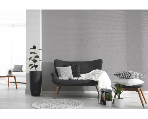 Grijs vliesbehang met bloemenpatroon in een lichte, modern ingerichte woonkamer met een donkere bank, kamerplanten en een wit tapijt.