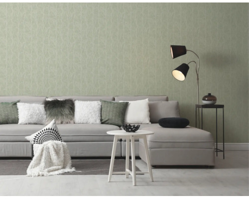 Moderne woonkamer met lichtgroen behang met takpatroon, grijze hoekbank, witte bijzettafel en een tweelamps vloerlamp.