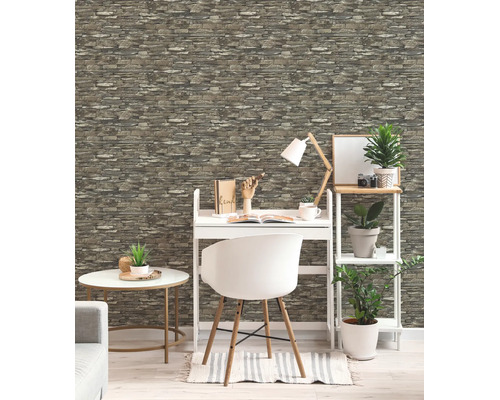 Heldere werkkamer met behang in steenlook, wit bureau, stoel, bijzettafel en stellingkast met groene planten.