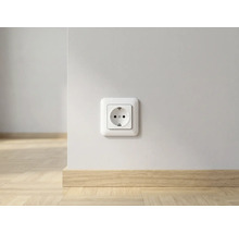 Stopcontact op een witte muur boven een lichte houten plint in een lichte kamer.