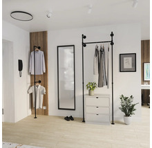 Open garderobesysteem van zwarte buizen in industrieel design in een lichte kamer met spiegel, ladekast en houten wandpaneel.
