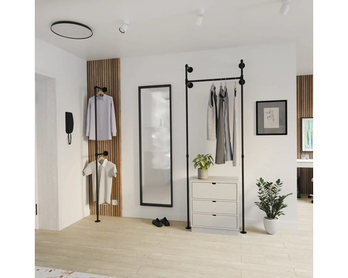Open garderobesysteem van zwarte buizen in industrieel design in een lichte kamer met spiegel, ladekast en houten wandpaneel.