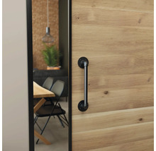 Houten schuifdeur met een zwarte deurgreep in industriële stijl, zicht op een eetkamer met houten tafel en zwarte stoelen.