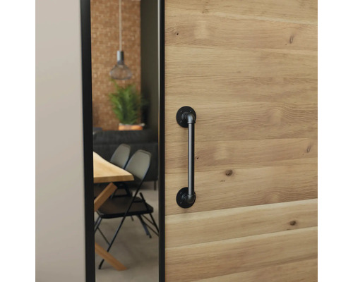 Houten schuifdeur met een zwarte deurgreep in industriële stijl, zicht op een eetkamer met houten tafel en zwarte stoelen.